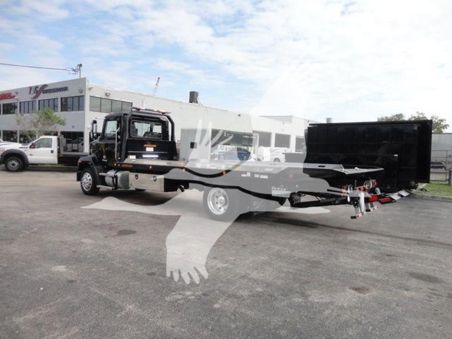 Truck in a dealership lot showing a Mack MD6 rollback wrecker configuration with extended bed and black equipment at the rear.