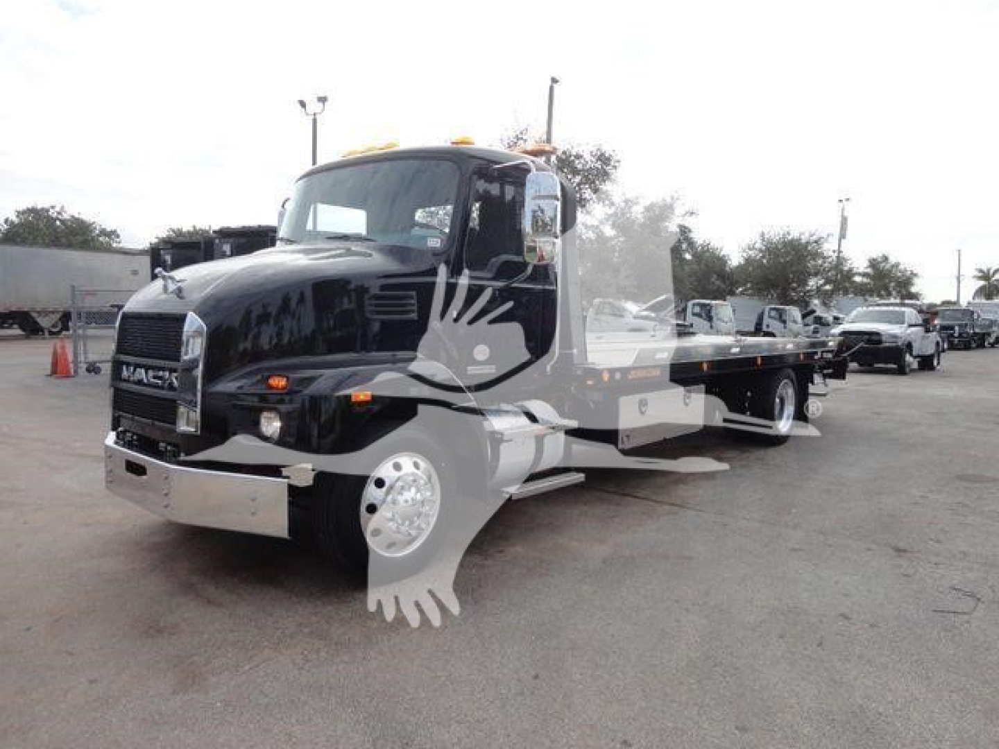 Tow truck: 2027 Mack MD6 rollback truck in black with chrome bumper, flatbed tow body, multiple amber warning lights on cab roof, warehouse lot background.