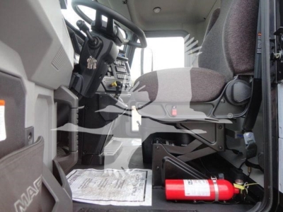 Cab interior of a 2027 Mack MD6 showing steering wheel, dashboard, driver's seat, and a red fire extinguisher under the seat.