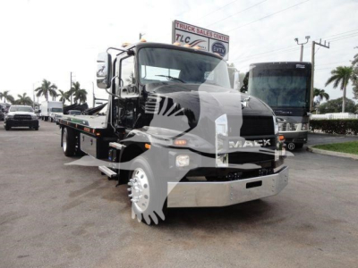 Mack MD6 rollback tow truck front view with flatbed, chrome bumper, and stock number sign in background.