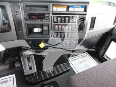 Cab interior of a 2027 Mack MD6 showing dashboard with radio, control panel, warning labels, and pedals.