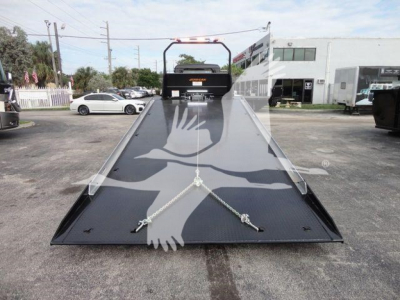Flatbed tow truck ramp with black steel deck and two chrome tie-down anchors, overhead guard rails, and center rear bumper, seen from front-of-bed angle.