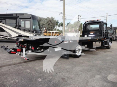 Flatbed rollback truck chassis in a dealership lot with a new Mack MD6 rolar image, showing long wheelbase and dual rear axles.