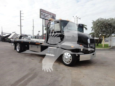 MD6 rollback truck in showroom setting, black cab with flatbed tow body, front chrome bumper, UNO white wheels, Mack badge visible.