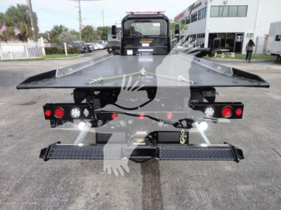 Flatbed tow truck chassis and rear view showing platform with taillights, rear step, and winch area on a new Mack MD6 rollback truck.