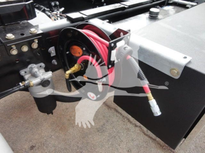 Close-up of Mack MD6 rollback truck front showing hydraulic hoses and reel with red hose and electrical connector.