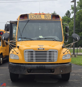 Yellow Freightliner Thomas school bus front view showing large grille, bumper, round mirrors, and 'SCHOOL BUS' sign on top.