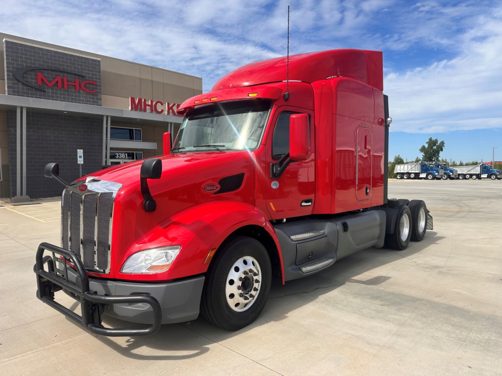 Peterbilt 579 tractor in red with black bumper guard parked in lot, front three-quarter view showing chrome grille and sleeper cab.