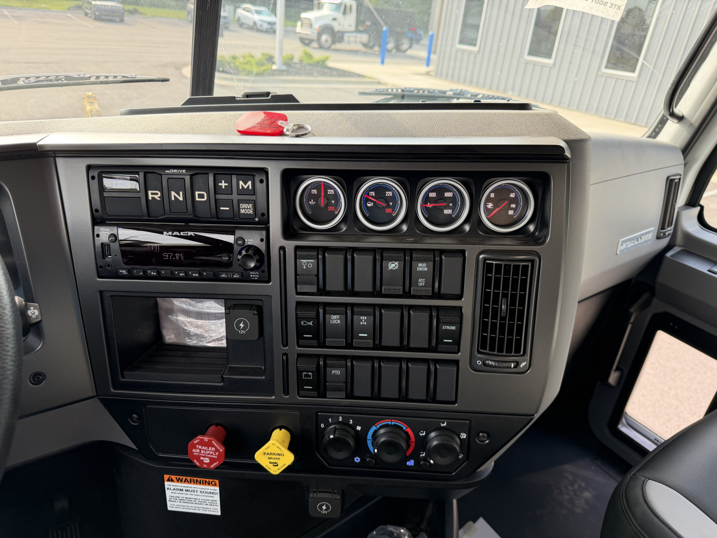 Dashboard of a 2027 Mack GR84F dump truck showing gauge cluster, HVAC controls, and radio with gear selector area.