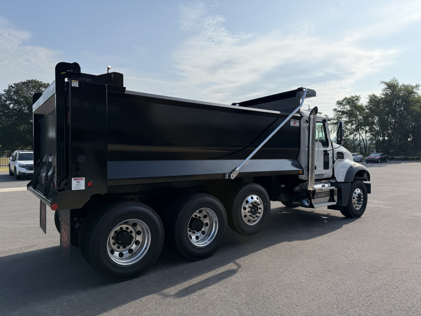 Dump truck side view showing large black dump body and white cab under clear sky.