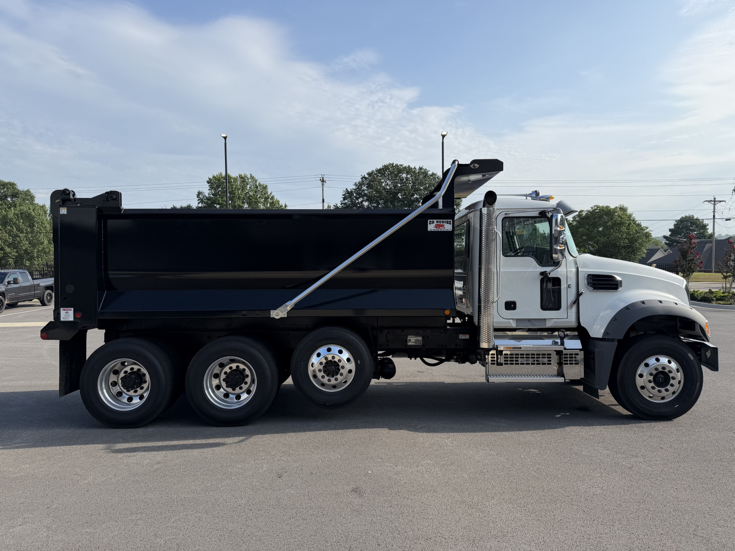Dump truck side view showing Mack GR84F chassis with black dump body and white cab. Visible text on cab door area and side panels includes brand and generic truck features. No engine details readable.