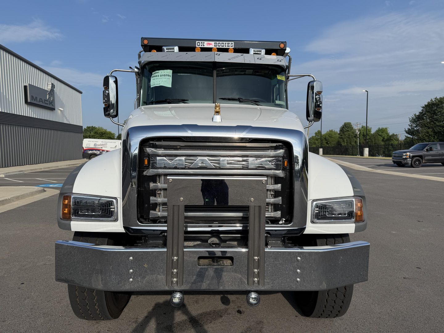 Truck front view of a white 2027 Mack GR84F dump truck with large grille, bumper guard, and towing hitch, displaying Mack emblem on grille.