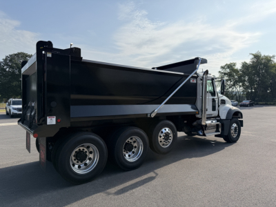 Dump truck side view showing large black dump body and white cab under clear sky.