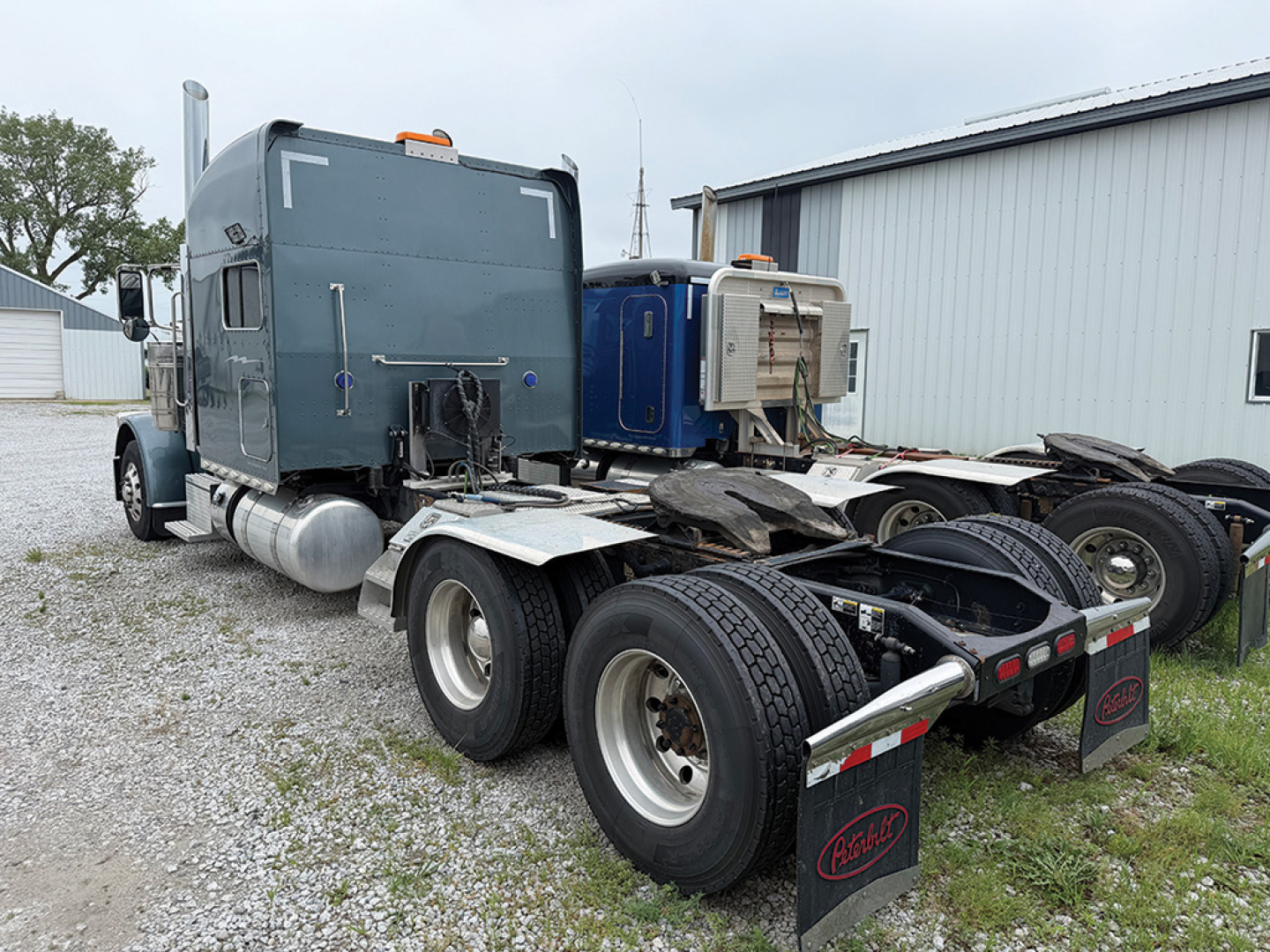 Peterbilt 389 UltraCab truck tractor left-side rear view showing fifth wheel and dual rear axles with mud flaps and fuel tanks.