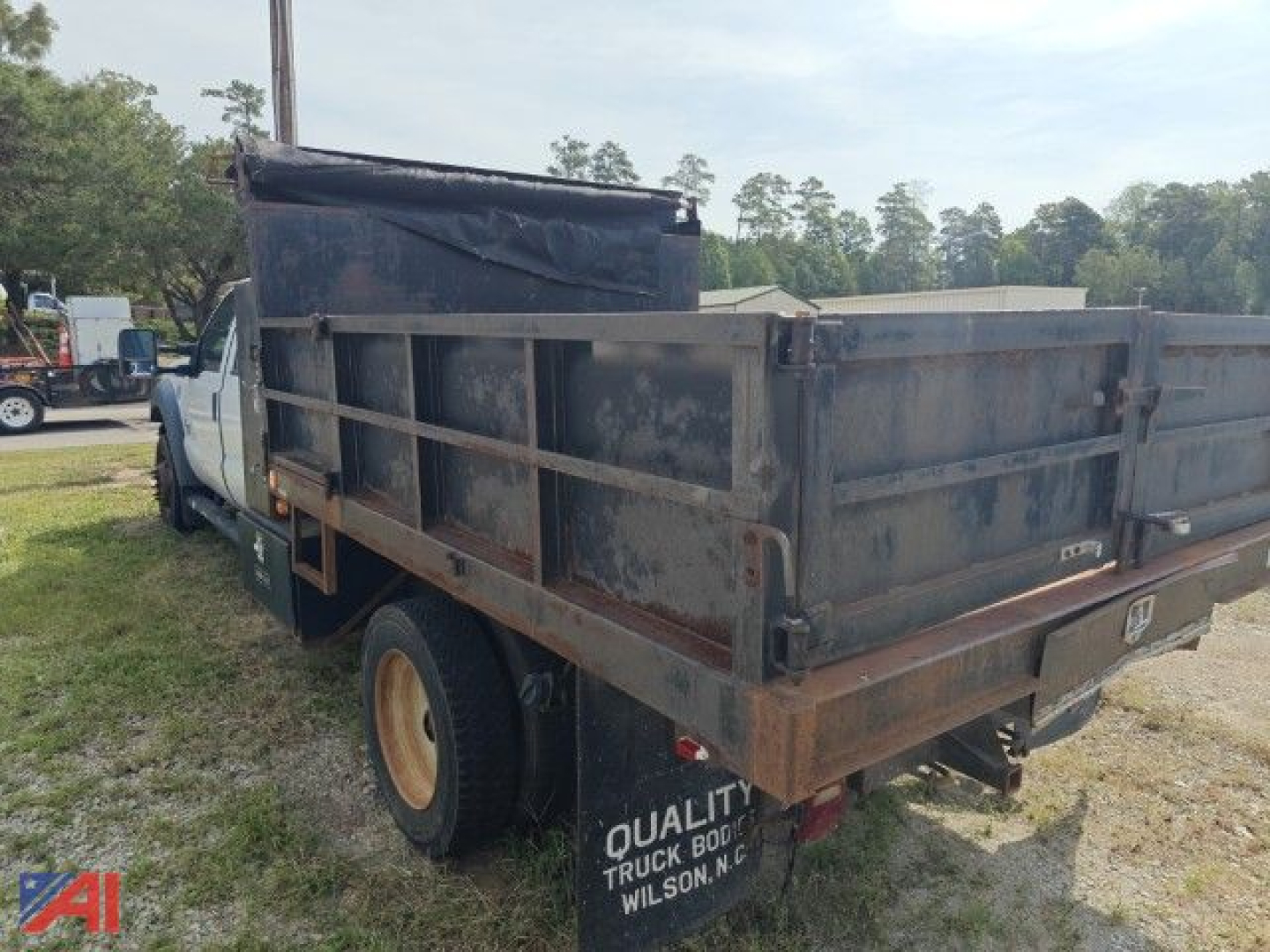 Dump truck bed in a Ford F-450 Super Duty with metal side panels and worn cargo bed, cab visible in background, rear view showing tailgate and wheel.