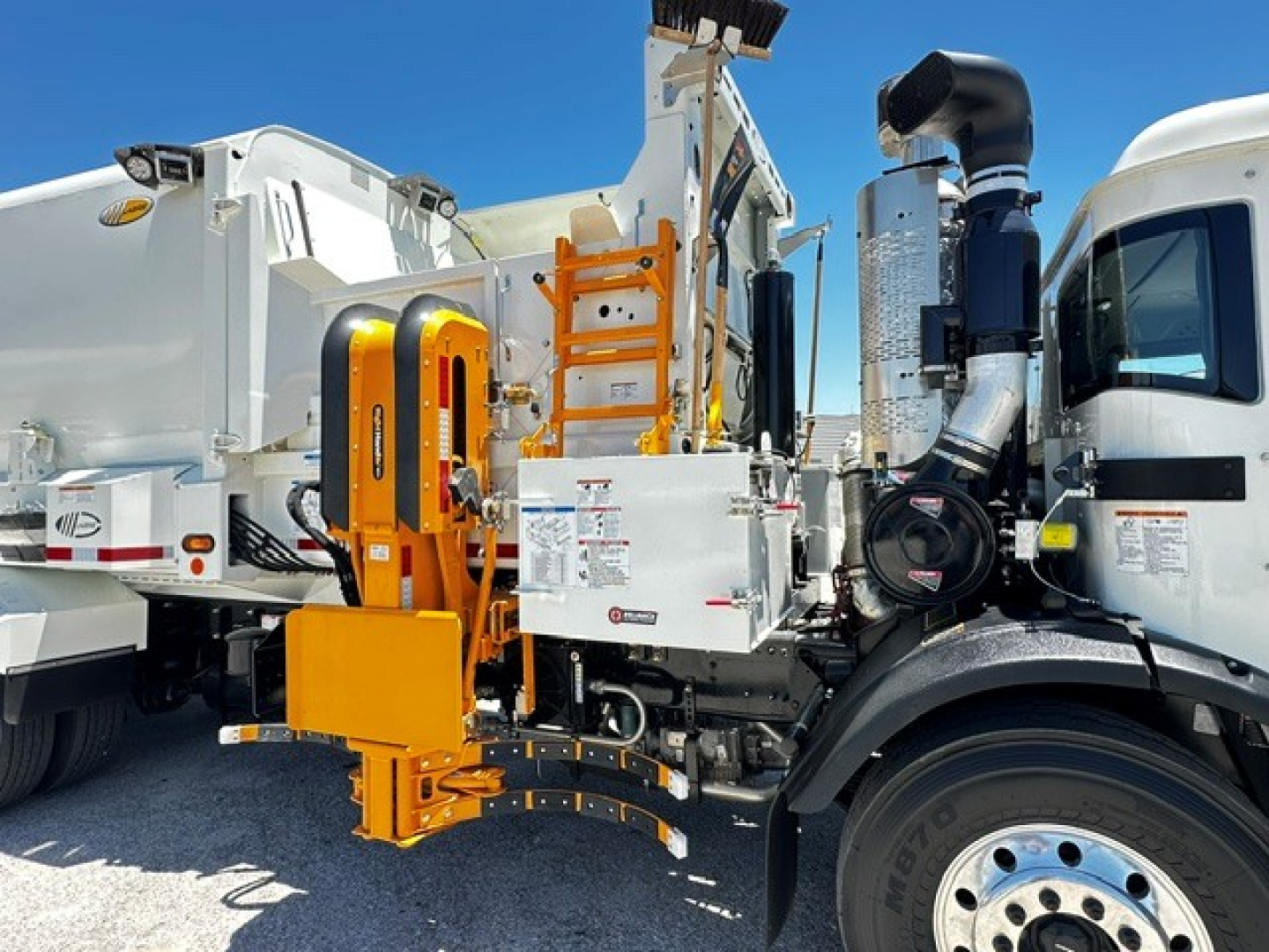 Truck cab with attached orange maintenance arm and equipment compartment, side view of a 2025 Mack LR64 sanitation truck.