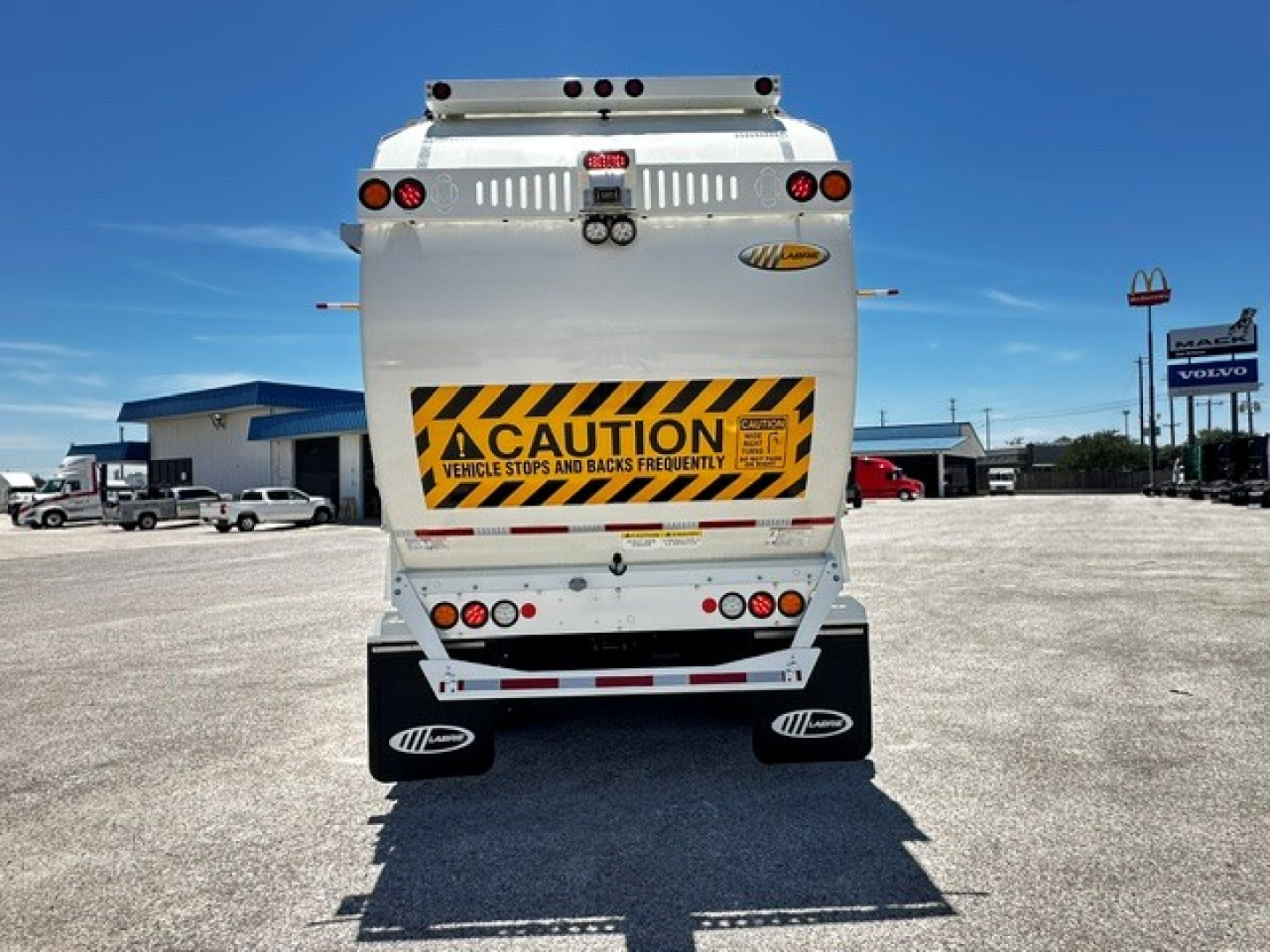 Back view of a white 2025 Mack LR64 garbage truck showing caution decal and rear lights.