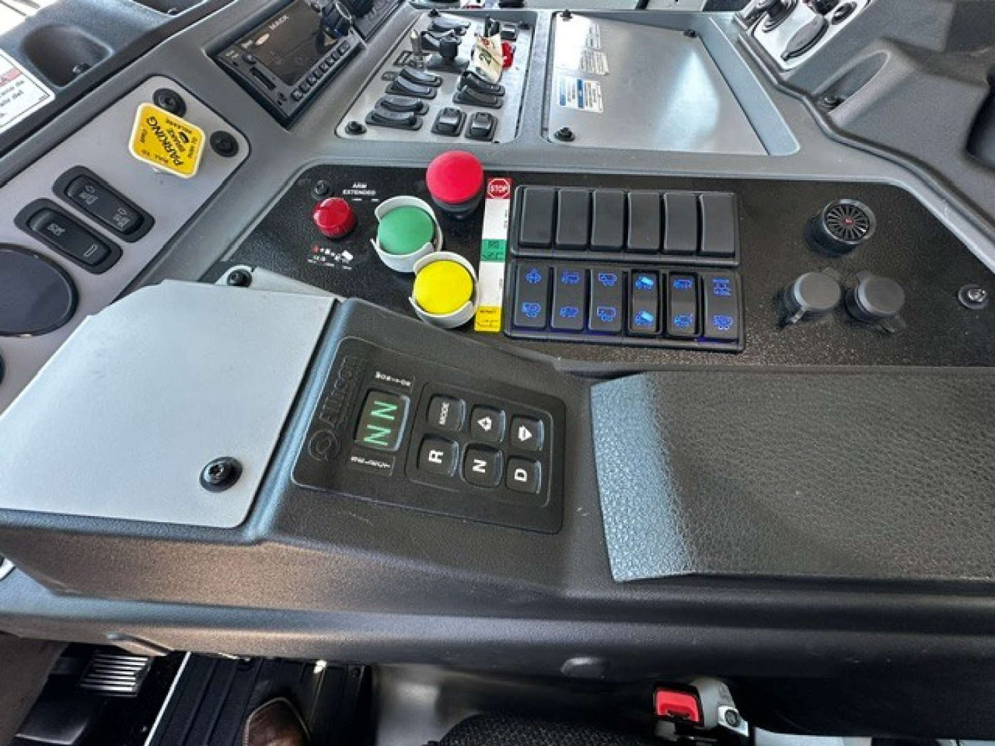 Cab control panel with colored push buttons and gear selector in a Mack LR64 truck cab, showing various switches and a digital display.