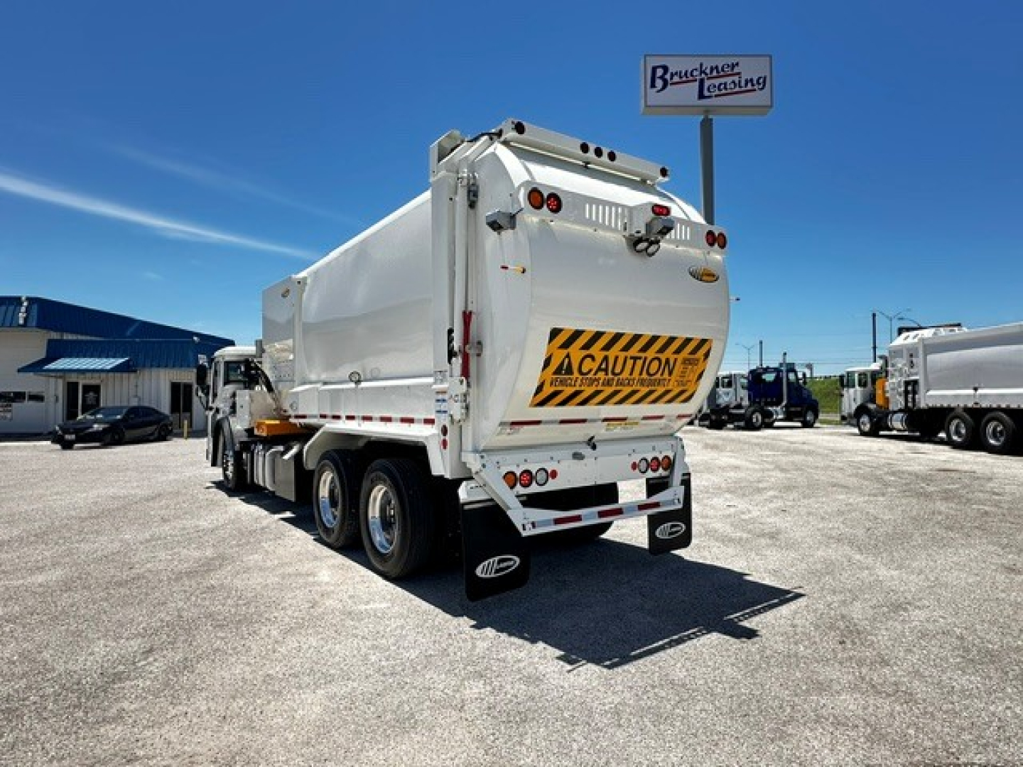 Mack LR64 dump truck rear view showing cargo bed with caution sign and taillights.