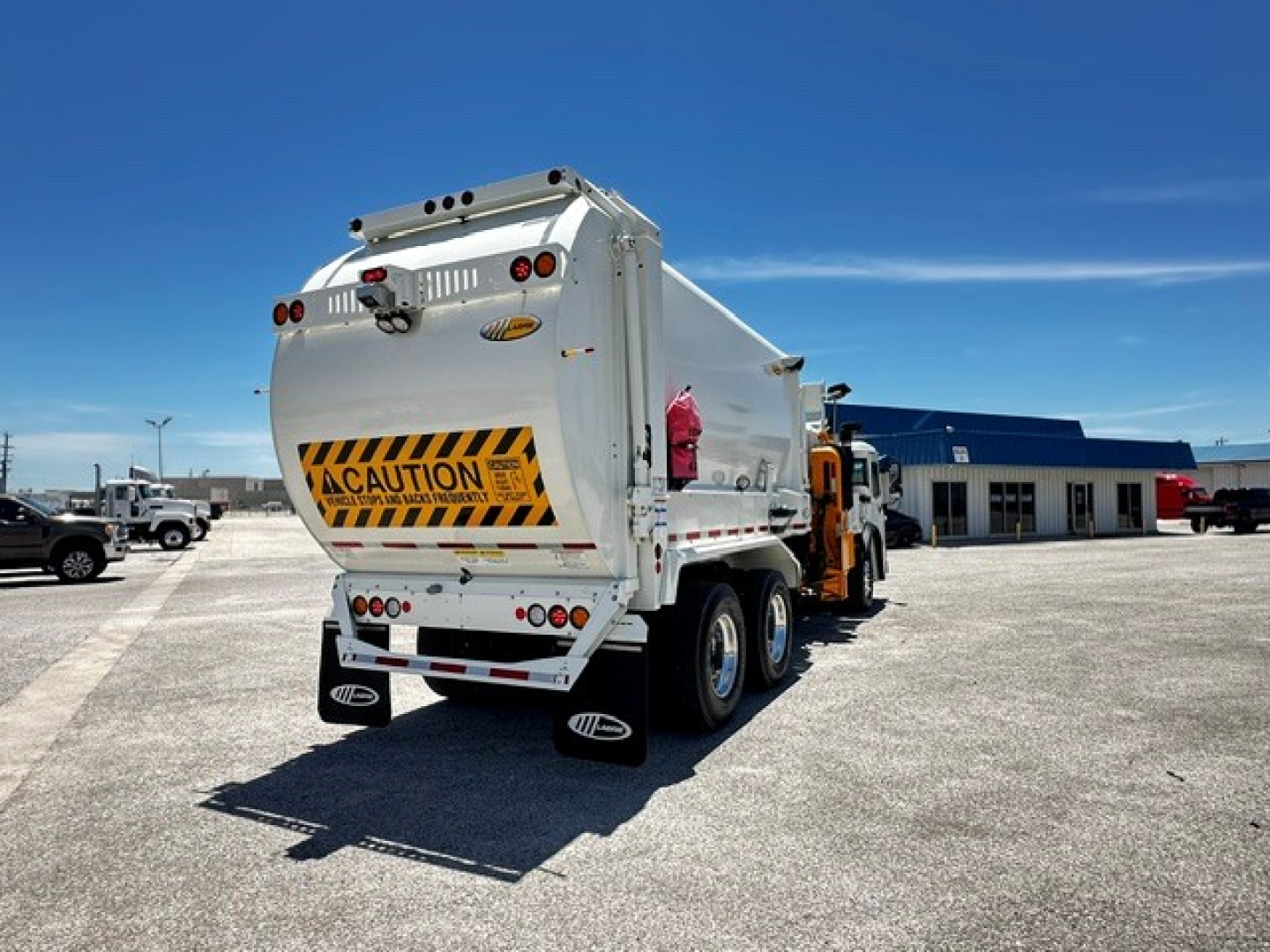 Rear view of a white Mack LR64 refuse truck showing CAUTION sign and rear lights.