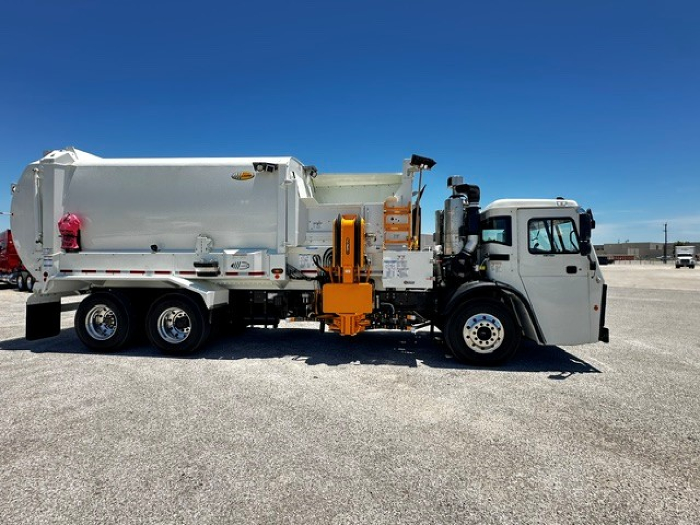 Mack LR64 refuse truck on level lot, side view showing large rear compactor body and orange hydraulic mechanism.