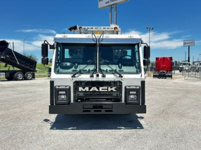 Front view of a white 2025 Mack LR64 truck showing grille with MACK lettering and bumper, with large windshield, mirrors, and rooftop lights.