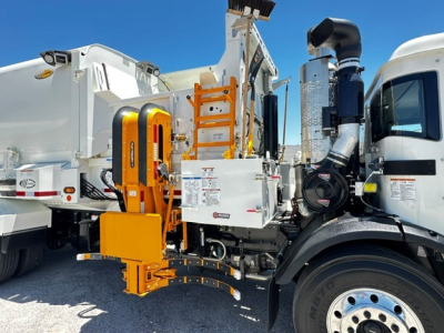 Truck cab with attached orange maintenance arm and equipment compartment, side view of a 2025 Mack LR64 sanitation truck.