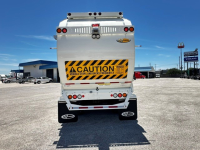 Back view of a white 2025 Mack LR64 garbage truck showing caution decal and rear lights.