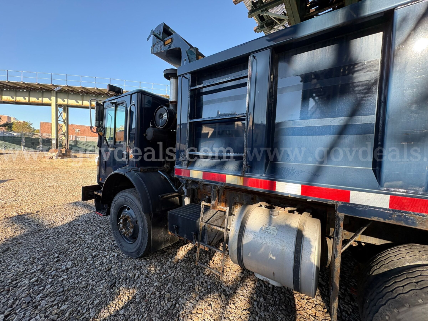 Dump truck side view showing hydraulic crane and rear dump bed on a Mack MRU600 with blue body and reflective stripe