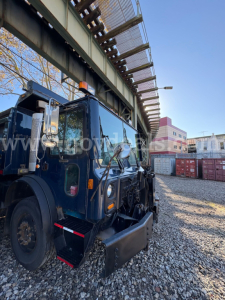 Front-left view of a blue Mack MRU600 dump truck in a yard with gravel, showing the cab and front equipment.