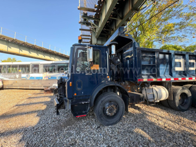 Mack MRU600 dump truck side view showing cab and hydraulic boom on blue body with black dual rear wheels and dump bed.