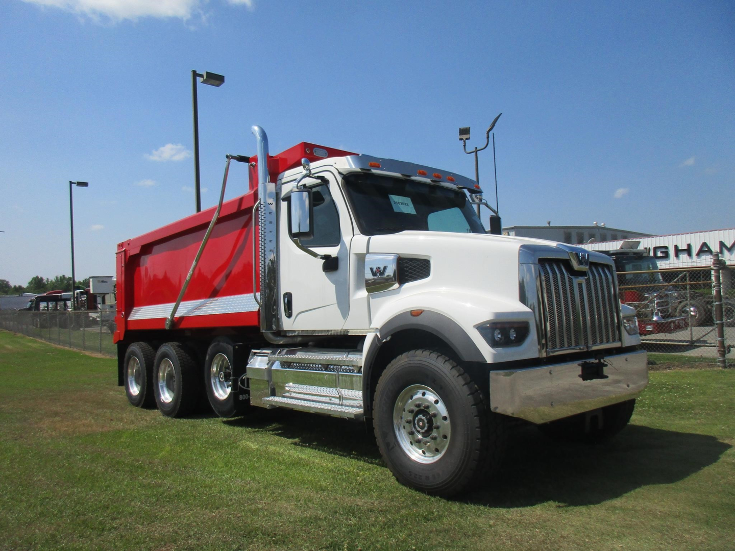 Western Star 49X dump truck in white cab with red dump body, side mirrors, chrome front bumper, and multiple axles on a dealership lot.