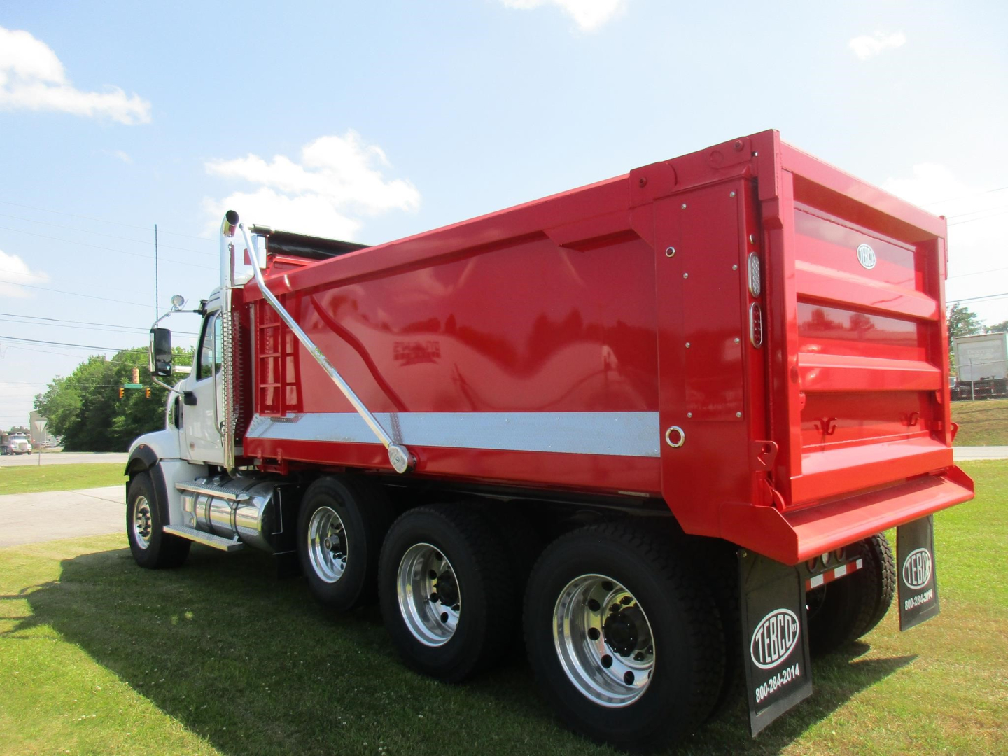 Western Star 49X dump truck in red with white reflective stripe, side view showing three-axle rear wheel assembly and dump bed.