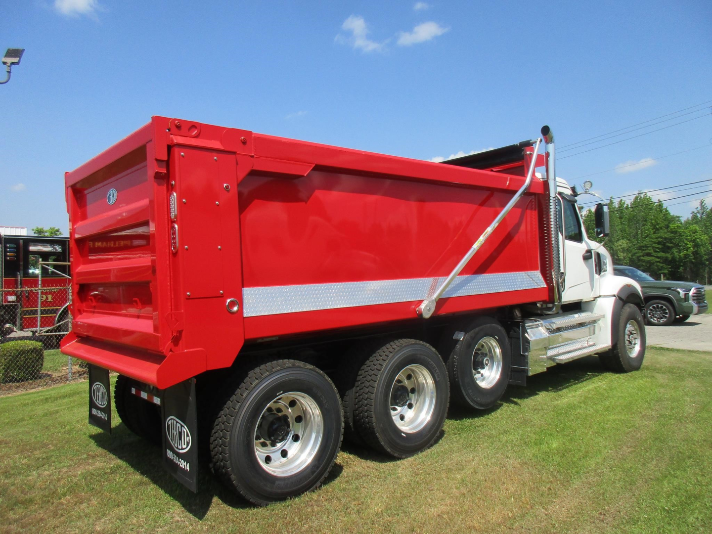 Dump truck bed of a new Western Star 49X with red dump body and chrome wheel rims, side view showing dual rear axles and hydraulic mechanism.