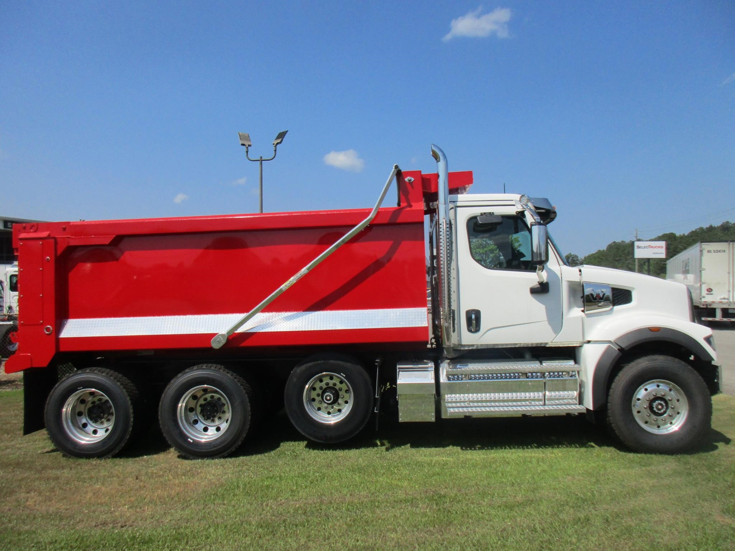 Western Star 49X dump truck side view showing red dump bed and white cab, dual rear axles, and chrome steps.