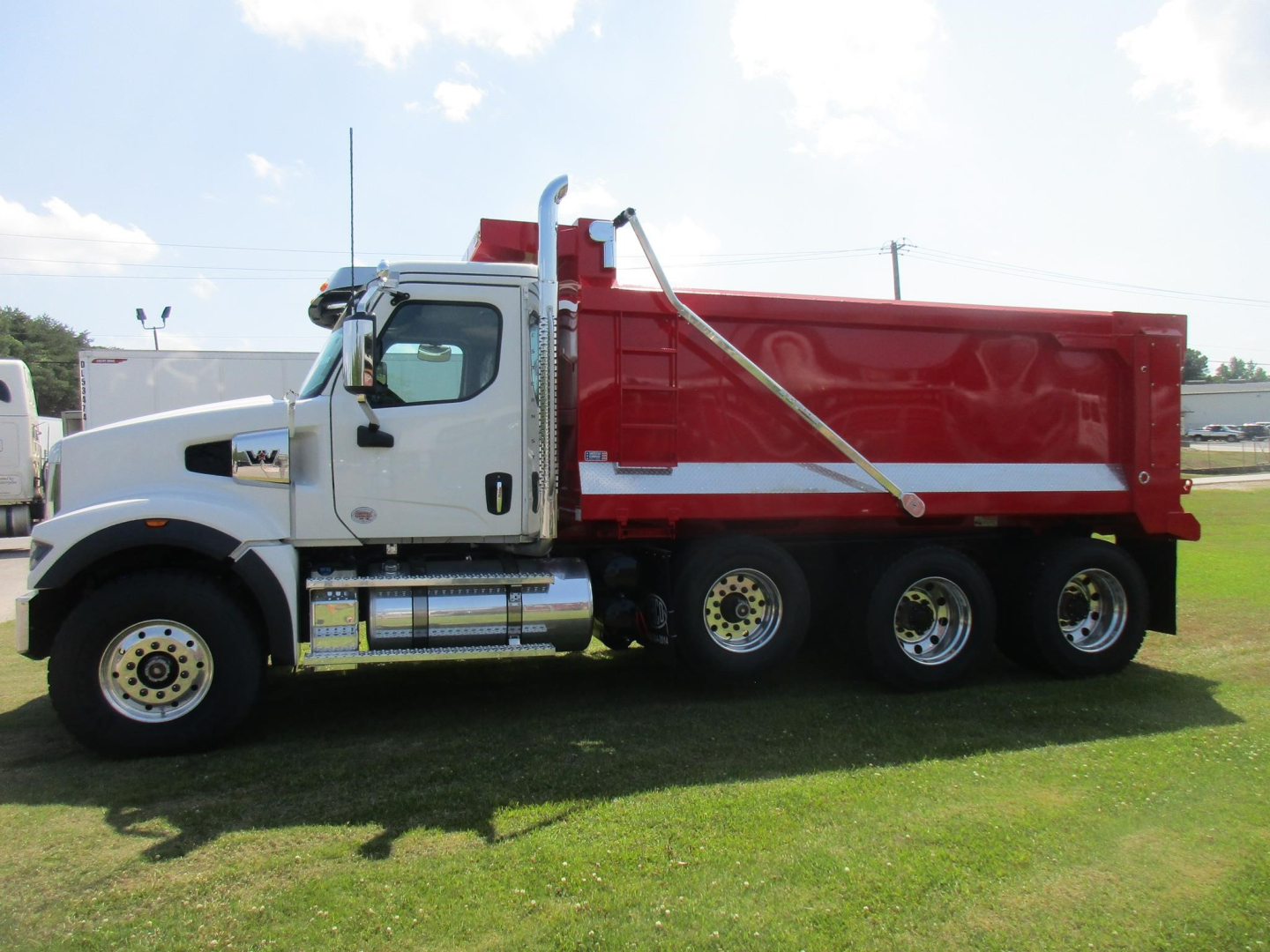 Western Star 49X dump truck side view showing white cab and red dump body with chrome fuel tanks and dual rear axles.