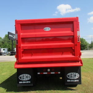 Rear view of a red dump truck body showing TEBCO logo emblems on the tailgate and mud flaps, with stock number bar and contact numbers on the mud flaps.