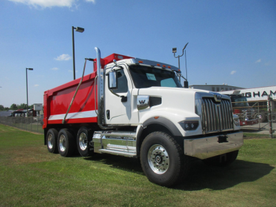 Western Star 49X dump truck in white cab with red dump body, side mirrors, chrome front bumper, and multiple axles on a dealership lot.