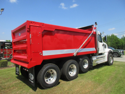 Dump truck bed of a new Western Star 49X with red dump body and chrome wheel rims, side view showing dual rear axles and hydraulic mechanism.