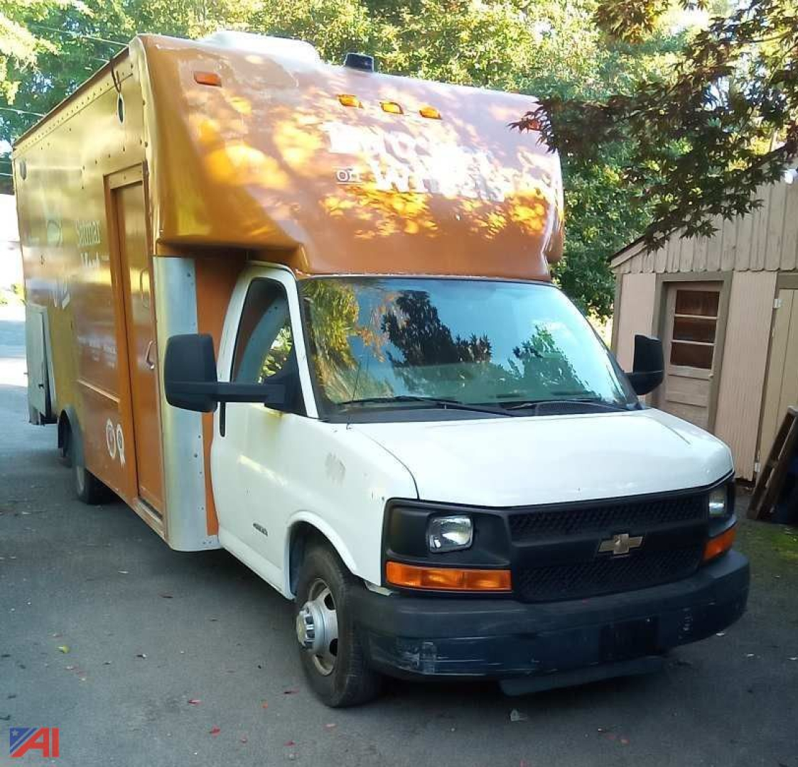 Food truck van in service with orange box body on a Chevrolet Express G4500 chassis, side view showing cab and cooking unit, 2014 model year.
