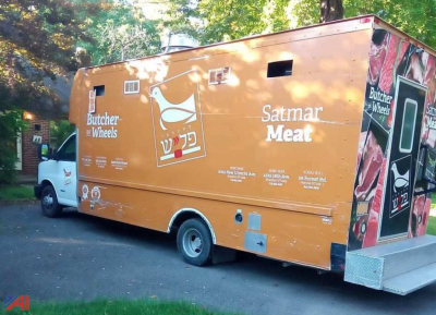 Food truck body with orange exterior, Chevrolet Express G4500 style cargo area. Side graphics show 'Satmar Meat', 'Butcher Wheels' and Hebrew text. Small windows and service/vent openings along side.
