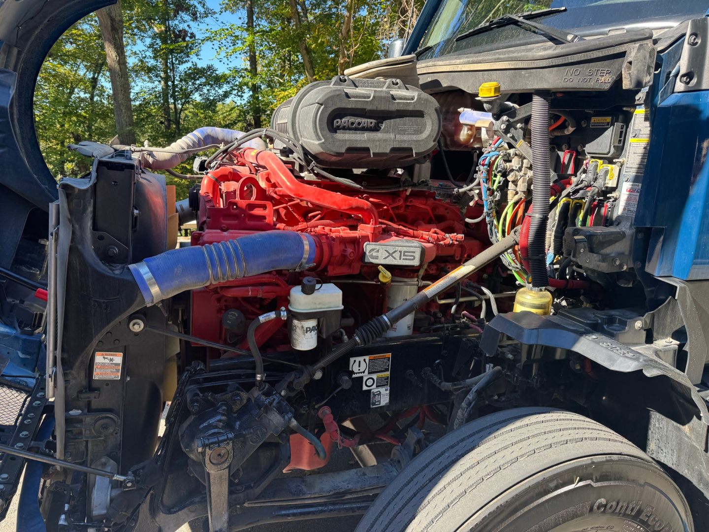 Kenworth T680 engine bay with red engine block, intercooler piping, air intake cover, and various hoses and wiring visible.