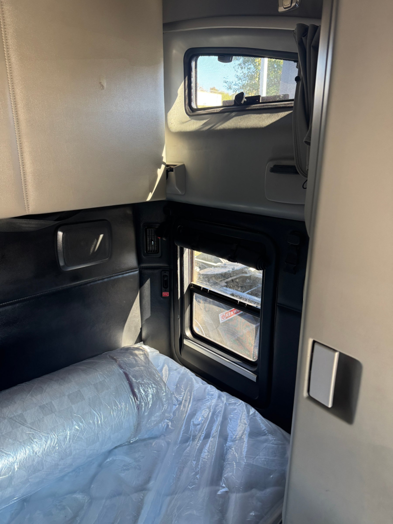Kenworth T680 sleeper cab interior showing cabin wall, window, doorway and a plastic-wrapped seat.