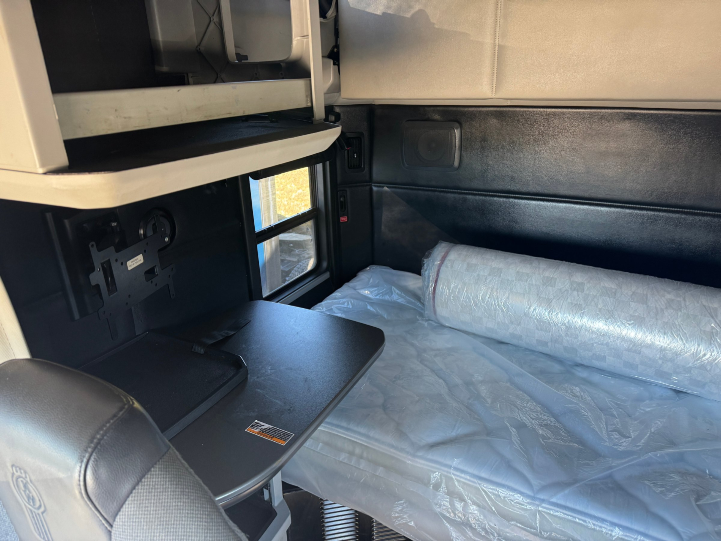 Kenworth T680 sleeper cab interior showing bunk bed area with a rolled mattress and small fold-out table.