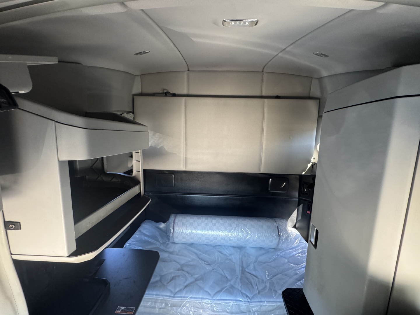 Kenworth T680 sleeper cab interior showing storage compartments and bed area with light gray upholstery