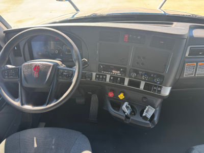 Kenworth T680 cab interior showing steering wheel with Kenworth emblem, dashboard controls, gauges, and ignition area with keys in ignition.