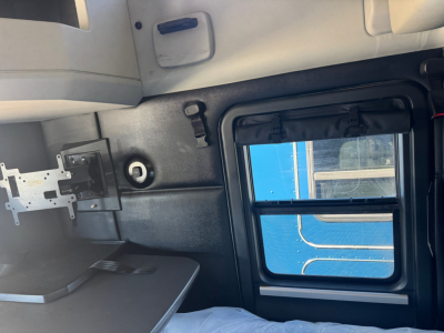 Kenworth T680 cab interior side panel with window and storage, showing a small circular vent and a mounting bracket.