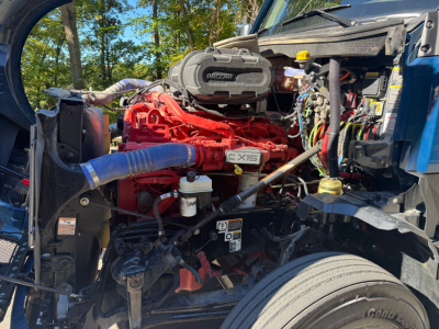 Kenworth T680 engine bay with red engine block, intercooler piping, air intake cover, and various hoses and wiring visible.