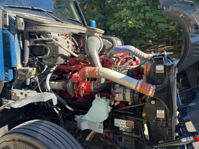Kenworth T680 engine bay showing red inline engine, orange intake manifold, white coolant reservoir, and label stickers.