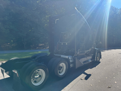 Truck cab of a 2024 Kenworth T680 tractor from the rear quarter showing dual rear axles and fifth-wheel area.